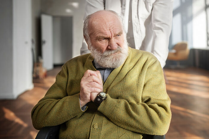 Elderly male patient with dementia in a wheelchair, wearing a green sweater, expressing an unfiltered and funny moment.