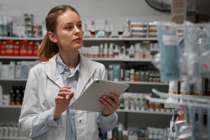 Female medical professional using tablet in pharmacy, reviewing strange health hacks shared by patients.