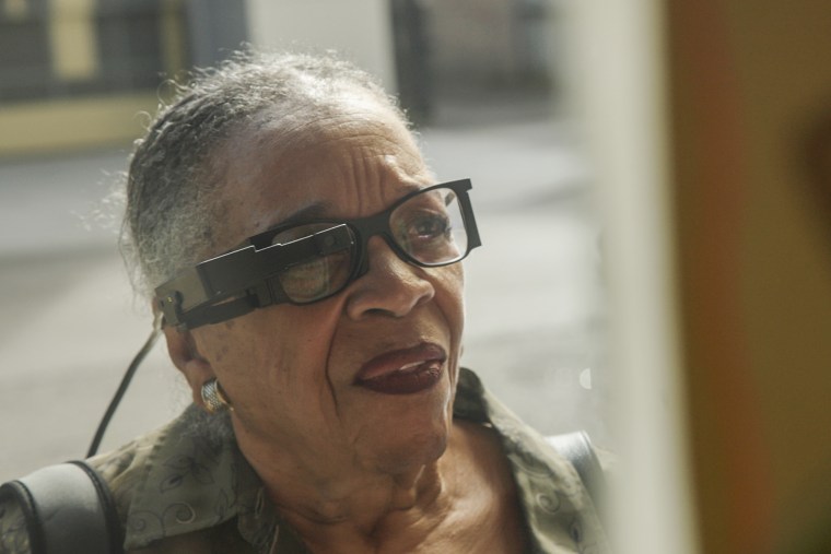 An old woman wears glasses with a device attached to one of the lenses