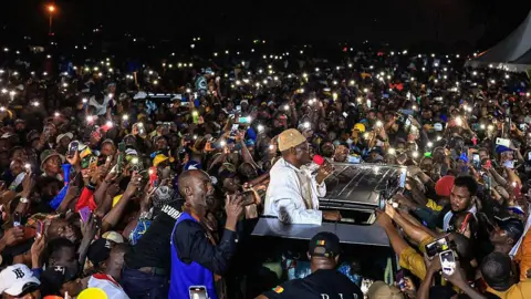AFP via Getty Images Supporters gather around Cameroonian presidential candidate Issa Tchiroma Bakary (C) during a campaign rally in Douala on 5 October 2025