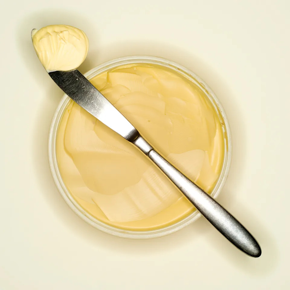 Butter in a round container with a spreading knife resting on top, holding a dollop