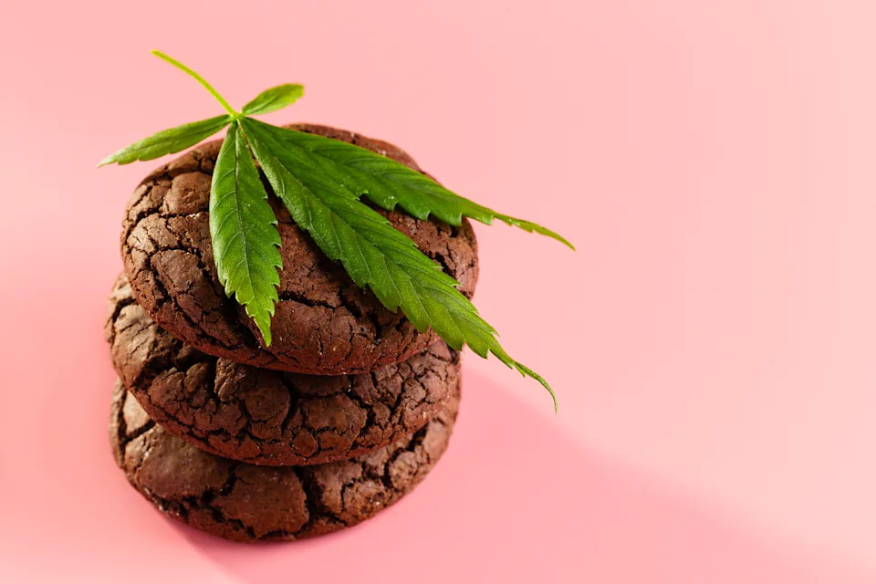 Stack of three chocolate cookies topped with a cannabis leaf on a light background