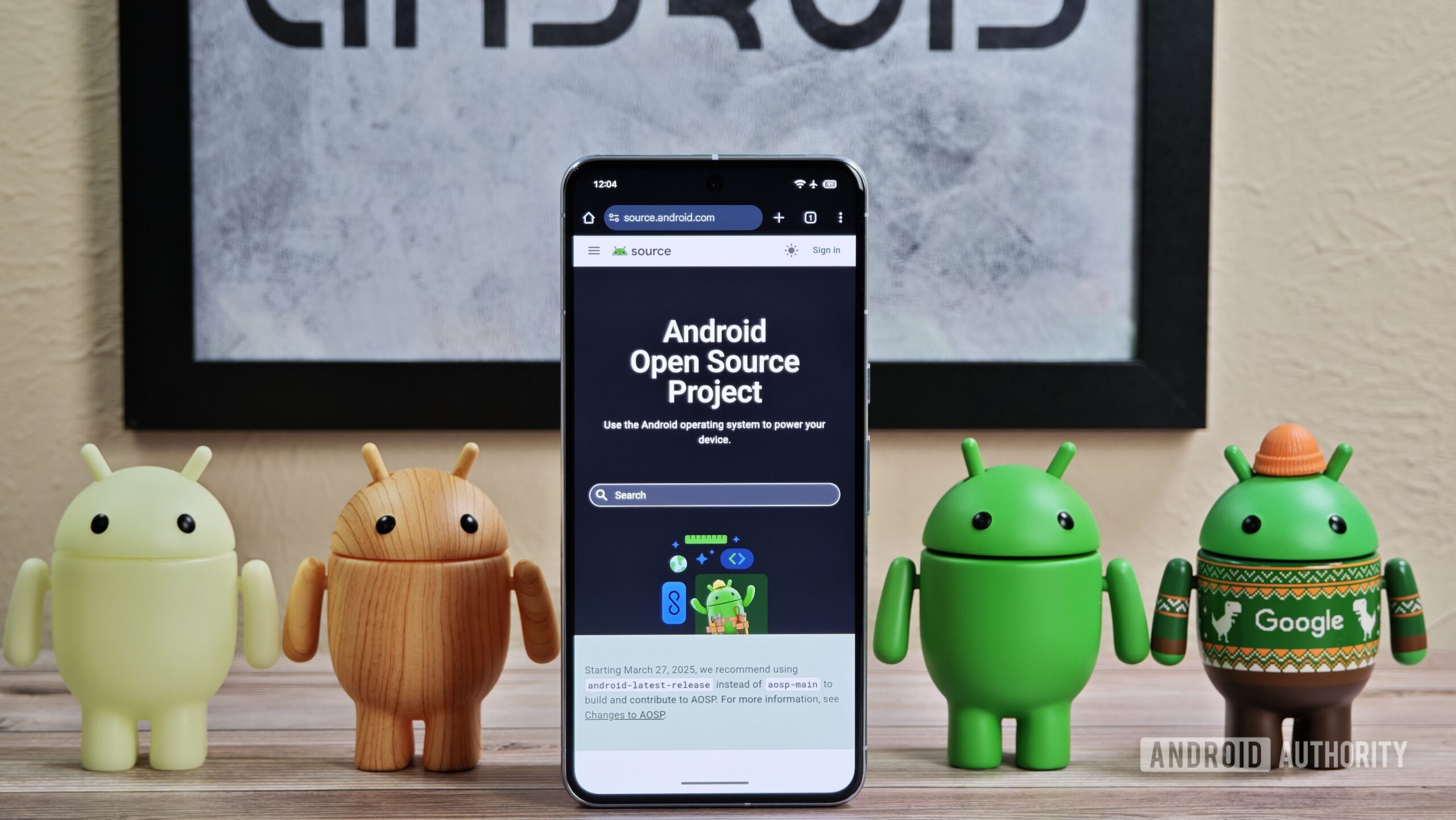 Android figures standing around Pixel phone with AOSP home page showing Android figures standing around Pixel phone with AOSP home page showing