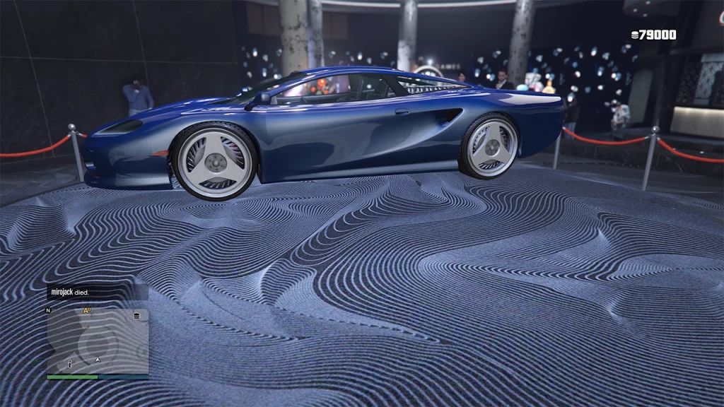 A metallic blue Ocelot Penetrator sports car is displayed on the Podium inside the Diamond Casino & Resort in Grand Theft Auto Online. The car is sleek and low-profile, sitting on a spinning circular platform covered in a dark, wavy patterned carpet. The casino interior is visible in the background with bright lighting and scattered people.