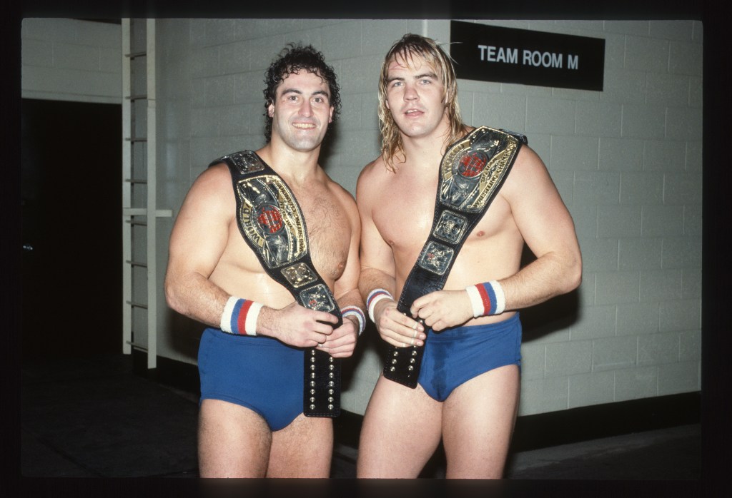 Team of wrestlers, with championship belts, pose backstage.Mike Rotunda and Barry Windham formed The U.S. Express.