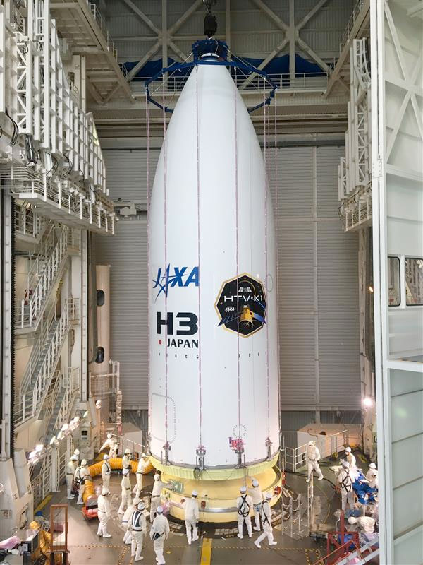 a conical white nosecone decorated with agency and mission logos is mounted atop its rocket