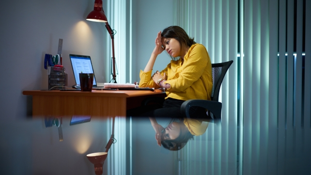 A person sitting at a desk while it's dark outside, looking tired and trying to study