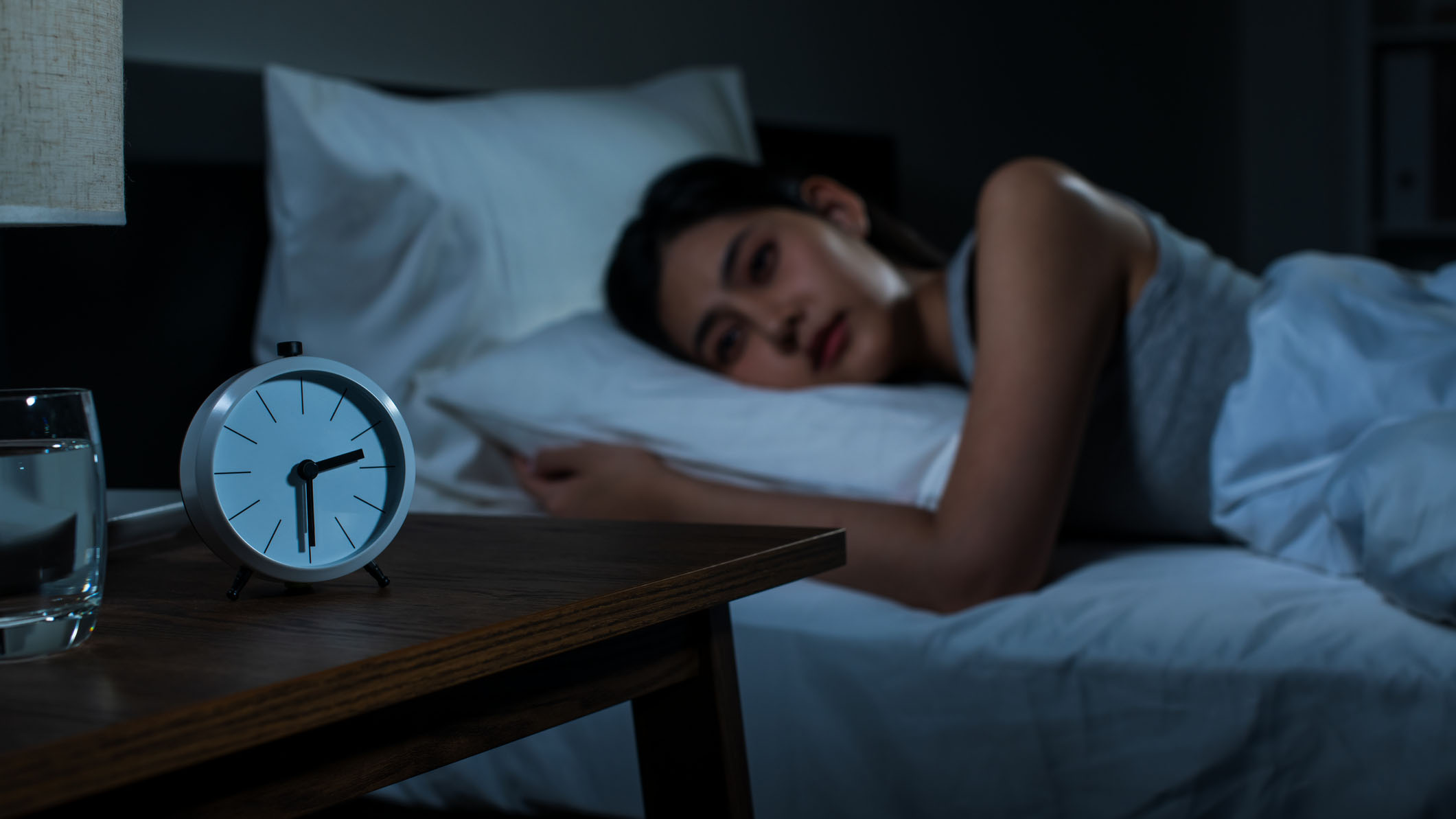 Women laying awake next to an alarm clock