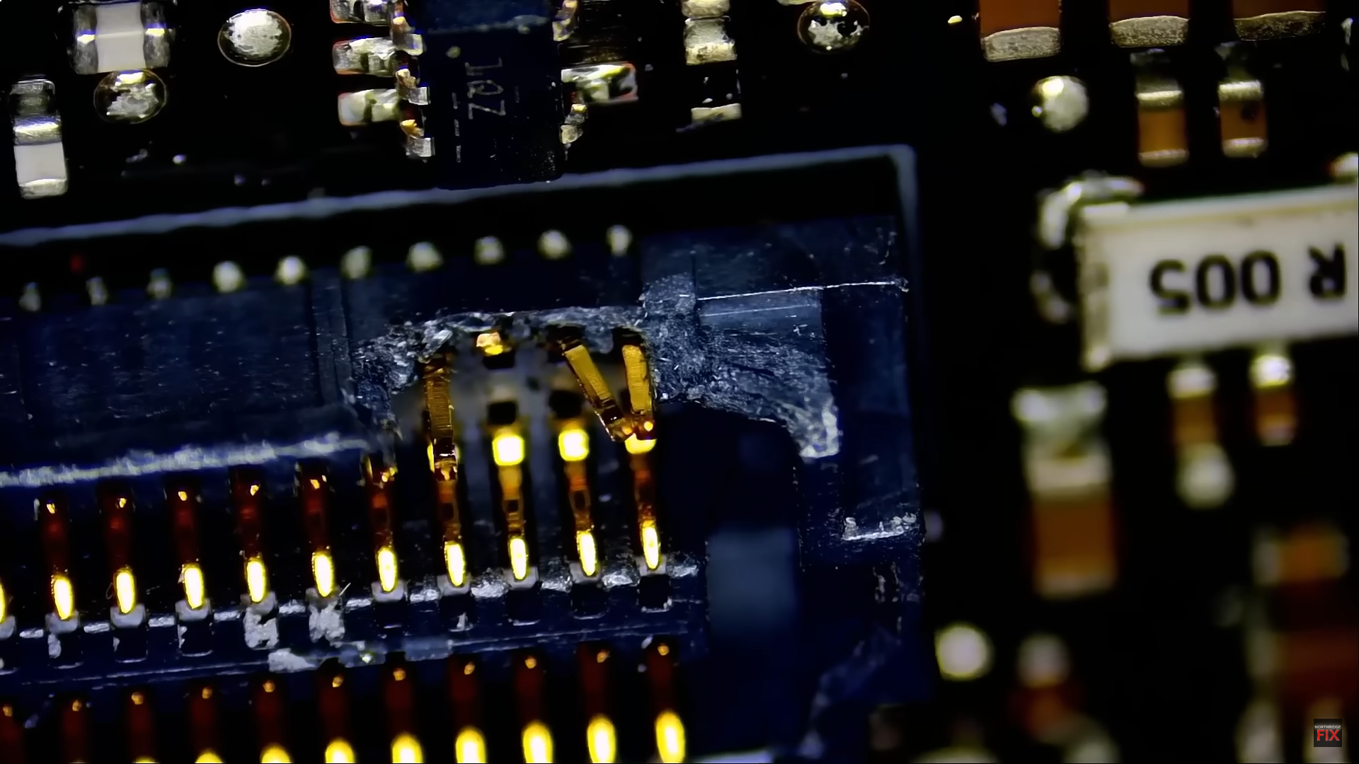 Close-up of a damaged circuit board with visible text R 005 and 1AZ.