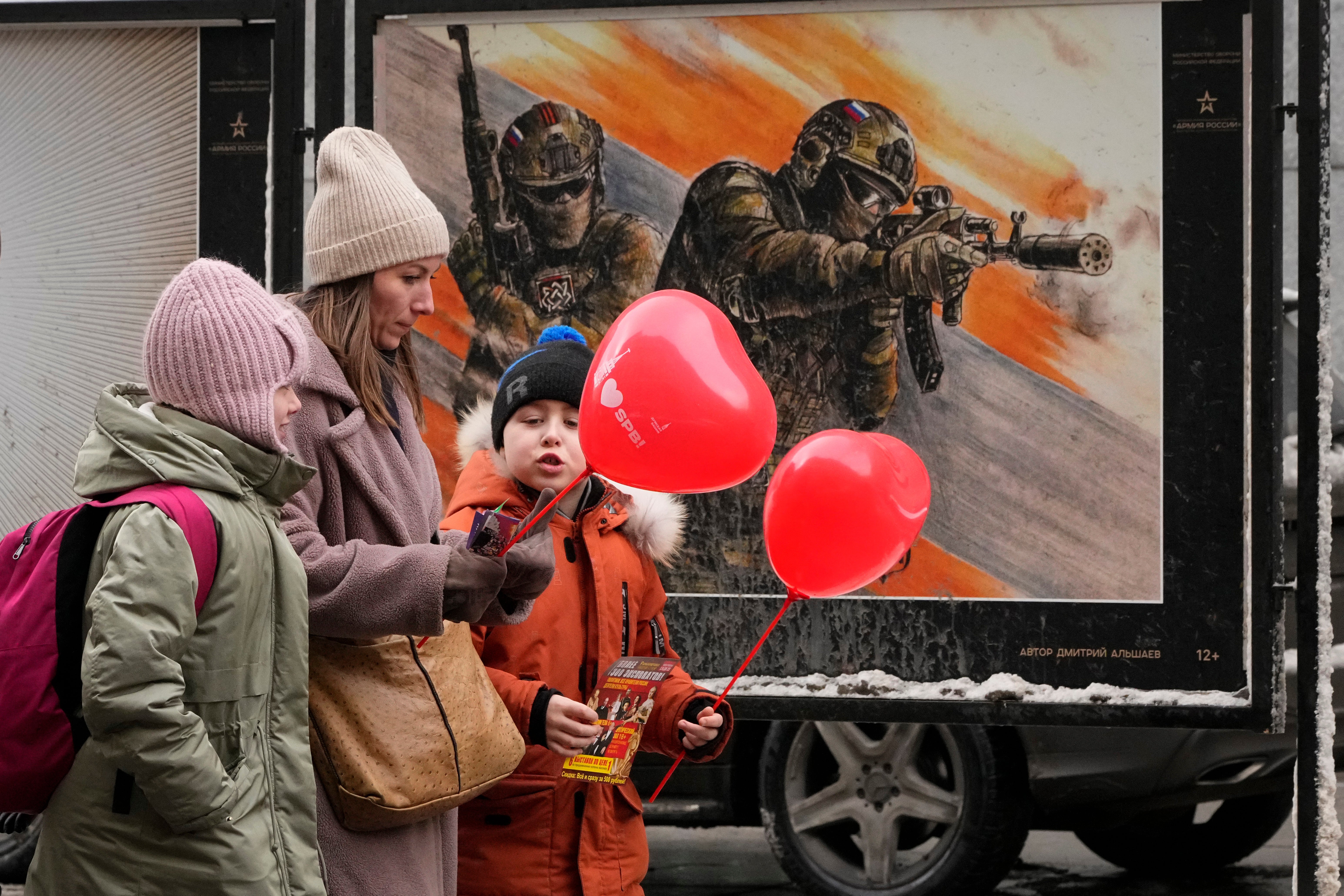A woman with two children walks past a street exhibition of military posters named 'Together to Victory' dedicated to Russian army in St. Petersburg, Russia, Friday, Feb. 14, 2025. (AP Photo/Dmitri Lovetsky, File)