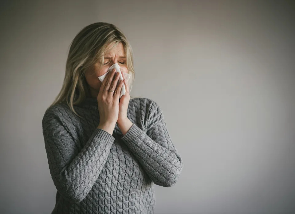 Person sneezing into a tissue, wearing a knit sweater, appearing to have a cold or allergies