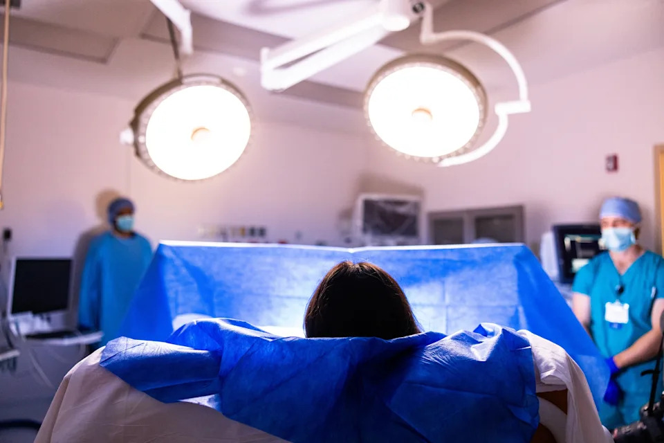 Medical professionals in surgical attire stand near a patient in an operating room with bright overhead lights