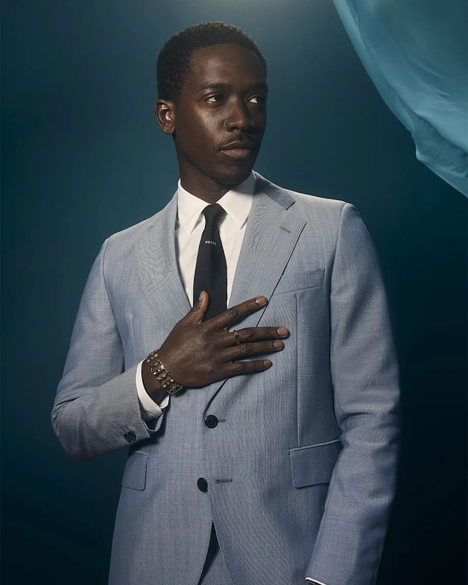 a person wearing a light blue suit with a black tie showing a formal pose