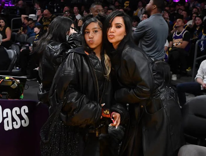 North West and Kim Kardashian pose for a photo at a basketball game, both wearing stylish, oversized leather jackets
