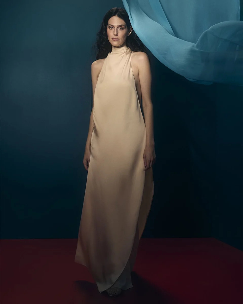a model wearing a halterneck gown standing against a colored backdrop