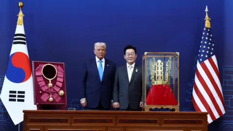 Reuters Donald Trump is presented with the "Grand Order of Mugunghwa" and a replica gold crown during a meeting with South Korean President Lee Jae Myung