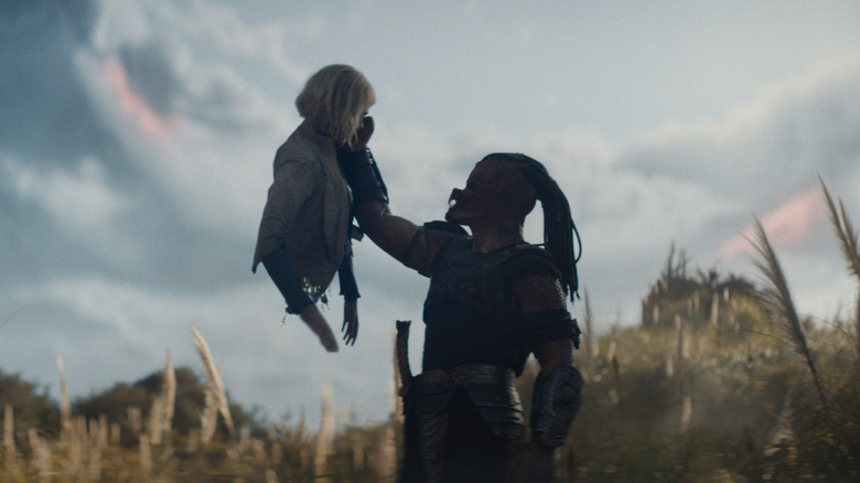 Dek holding up Thia's head and torso against an alien sky backdrop in Predator: Badlands