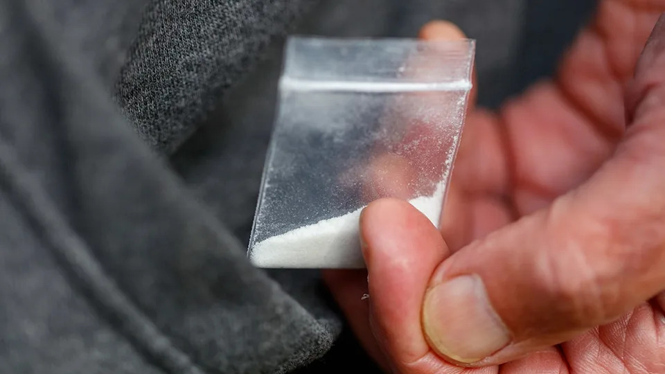 hand holds white powdered fentanyl drugs in small bag