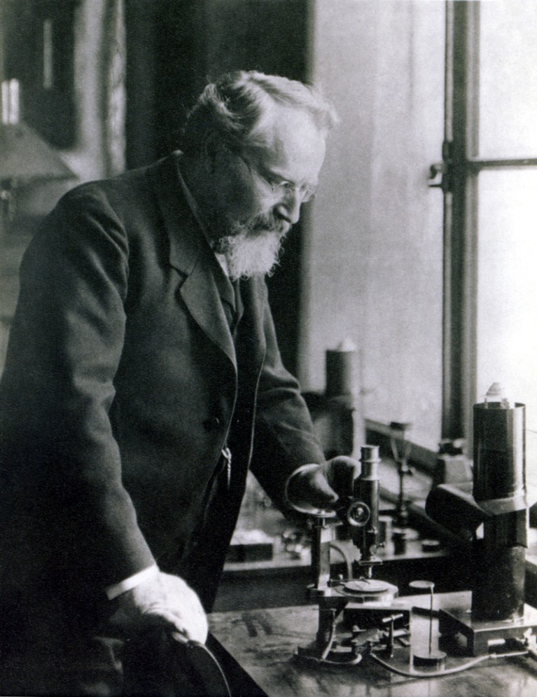 Black and white photograph of Otto Lehmann standing at a bench using a microscope.