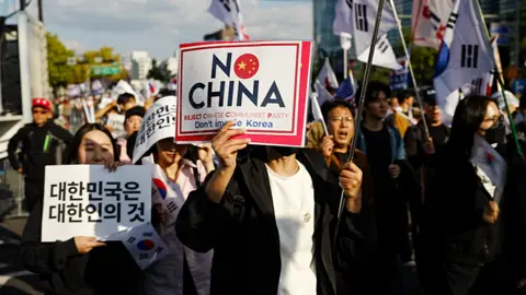 A man, a woman and others in the protest hold up slogans that read 'No Trump'.