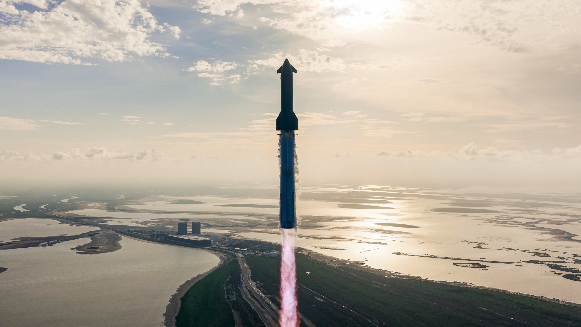 a huge rocket launches into the sky with wetlands and a calm ocean in the background