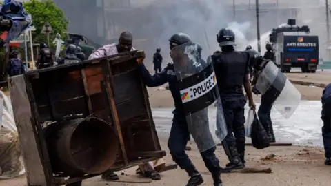 Reuters An anti-riot police officer removes a barricade during clashes with supporters of Cameroon presidential candidate Issa Tchiroma, after the Constitutional Council declared President Paul Biya the winner of the October 12 presidential election, in Douala, Cameroon, October 27, 202
