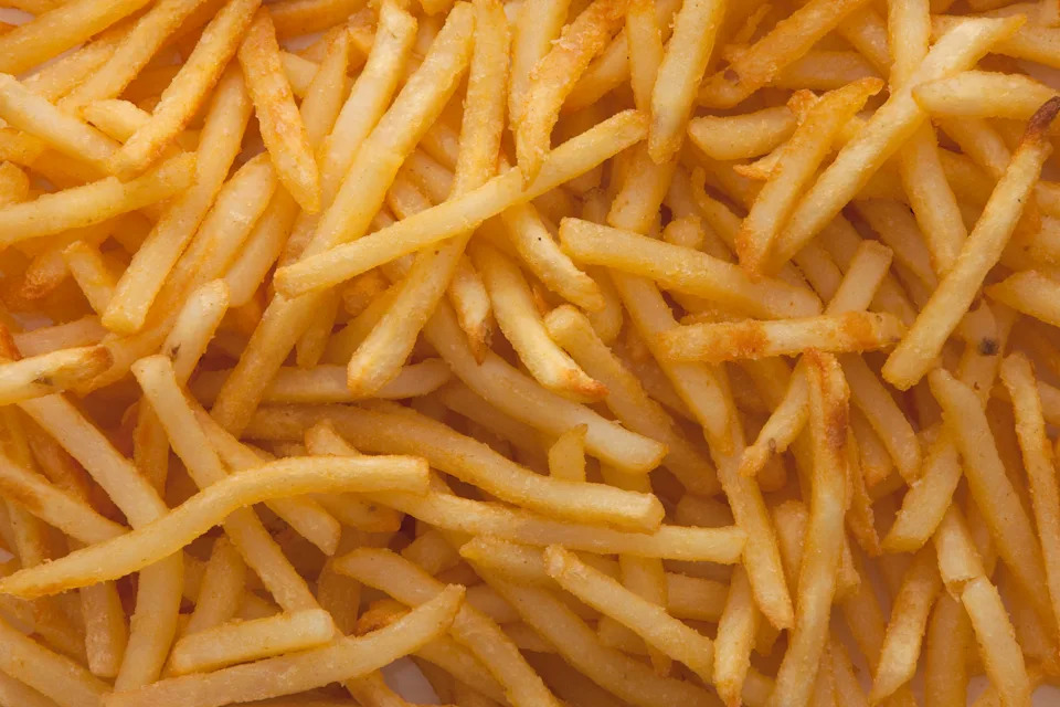 A large pile of crispy French fries fills the image, showcasing their texture and golden-brown, appetizing appearance