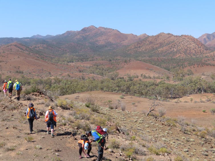 A group of people in high-vis clothing walk across a rocky red landscape.