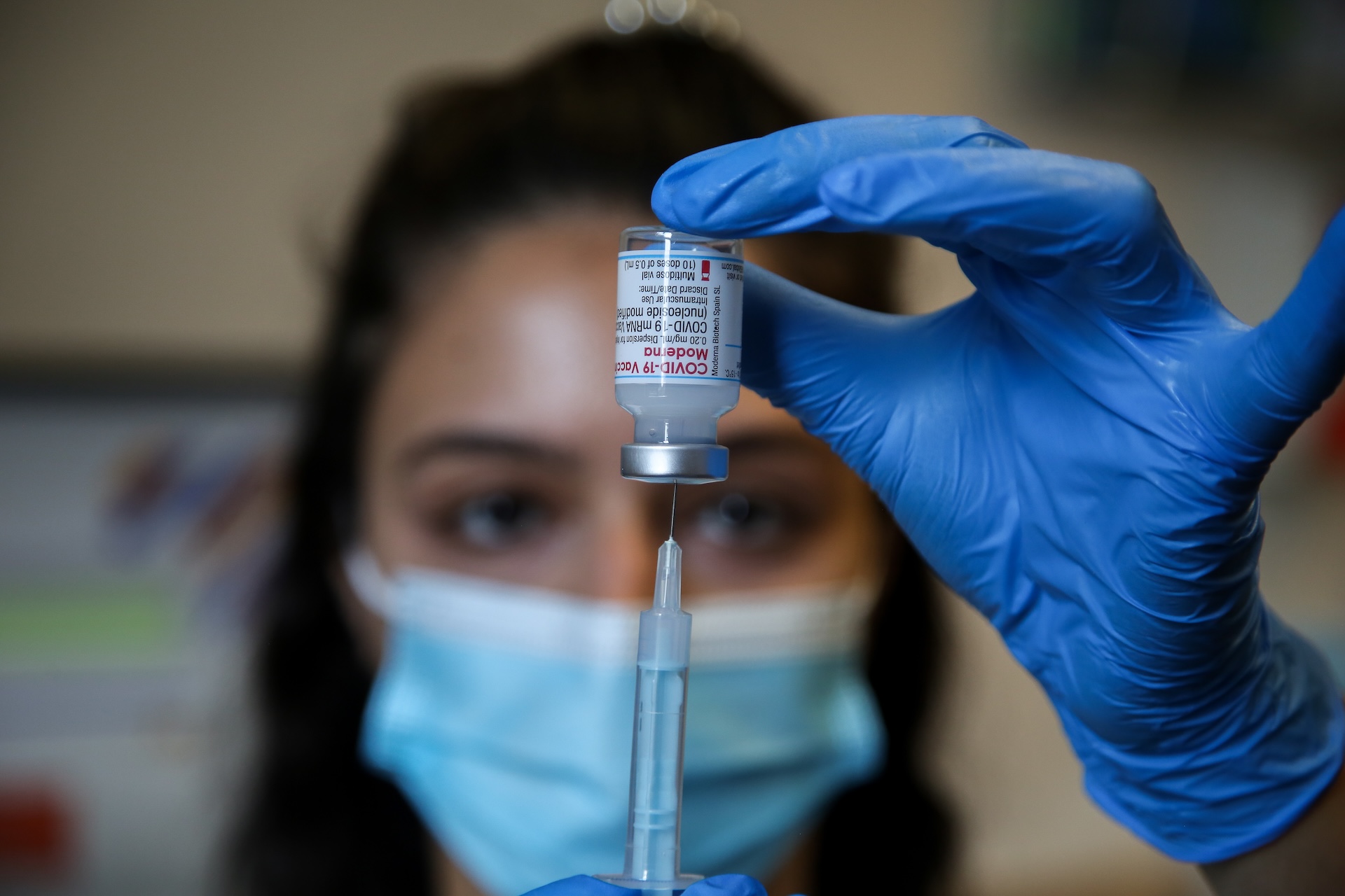 a healthcare worker withdraws a dose of COVID-19 vaccine from a vial