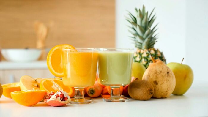 Two glasses of fresh fruit and vegetable juice surrounded by whole fruits highlighting strange and dumb health hacks.