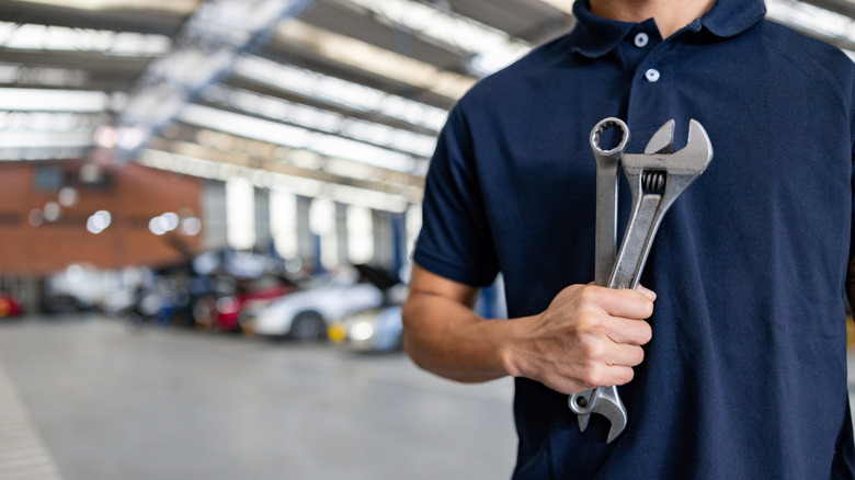 A mechanic holding wrenches with vehicles in the background