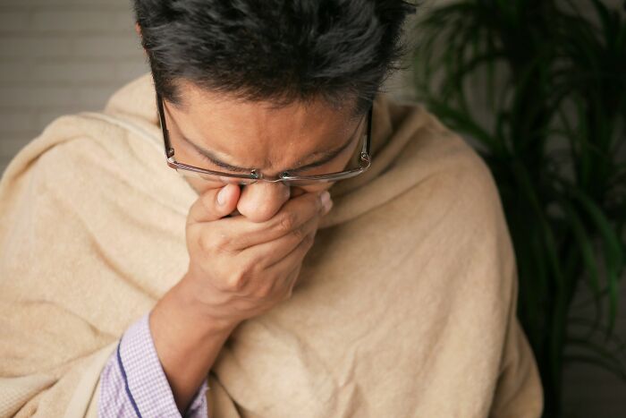 Man wrapped in a blanket coughing into his hand, illustrating strange and dumb health hacks shared by patients.