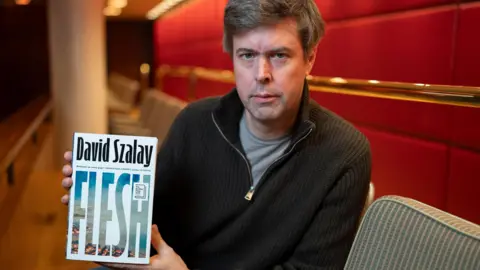 Getty Images David Szalay holding up the cover of his novel Flesh