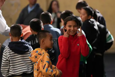 Getty Images Children play on the street during an event to mark the 70th anniversary of the establishment of Xinjiang as an autonomous region of China. In the foreground are a boy in an orange, patterned jacket and a girl in a red sweater gesturing with both her hands