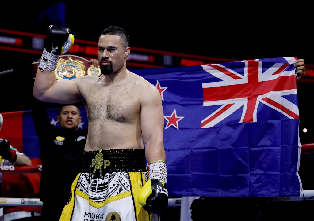 Boxer Joseph Parker in the ring, holding up a championship belt and a New Zealand flag.