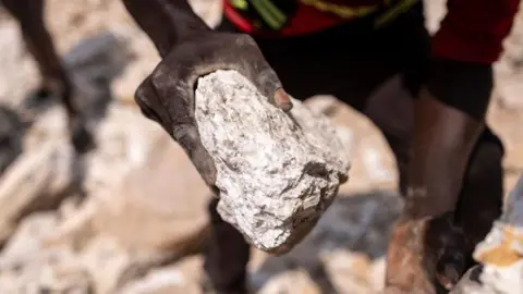 AFP via Getty Images A miner holding a rock that contains lithium at a mine in Nigeria