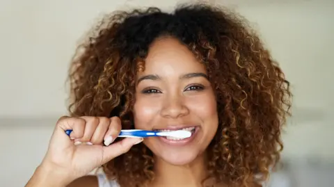 Getty Images Woman smiling and brushing her teeth