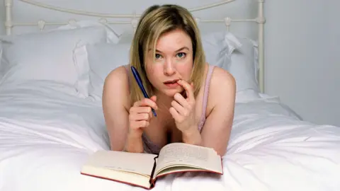 Alamy Bridget Jones - Renee Zellwegger in character, lying on a bed writing her diary.