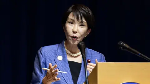 EPA/Shutterstock Takaichi in a blue blazer speaking at a podium.