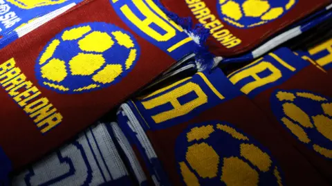 EPA FC Barcelona maroon and blue scarves layered on top of a table at a stall outside a stadium.