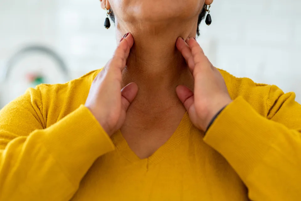 Person performing a self-massage on their neck and throat, wearing a knit sweater and dangling earrings