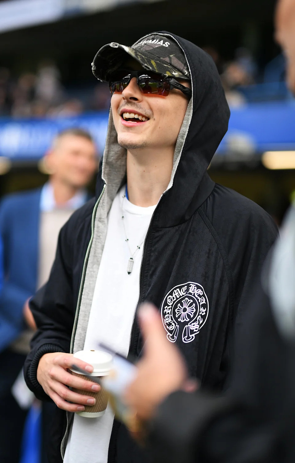 Timothée outdoors with a casual hoodie, cap, and sunglasses