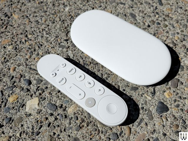 Small white remote with a few buttons beside a flat, white, elongated disc-shaped device