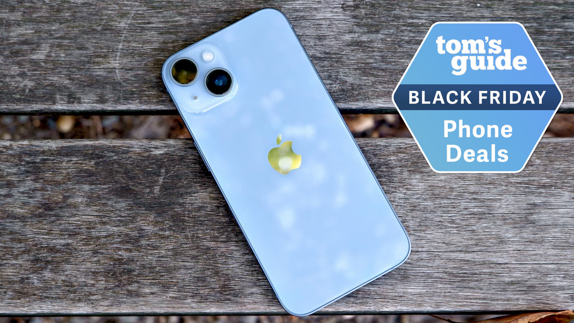 iPhone 14 on wooden surface with Black Friday badge nearby.