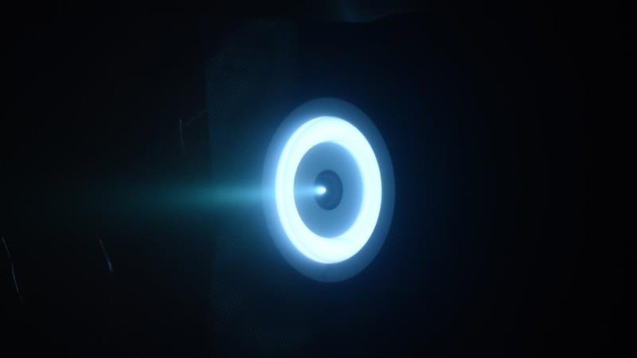 a bright blue-white ring of light on a black background, with a plume of bright white gas ejecting from a nozzle in its center