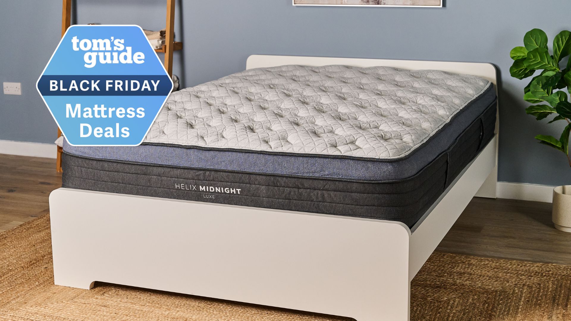 The image shows a white mattress with a dark blue and black trim placed on a white bed frame in a neutrally decorated bedroom. A 'Tom's Guide Black Friday Mattress Deals' badge is overlaid on top of the image.