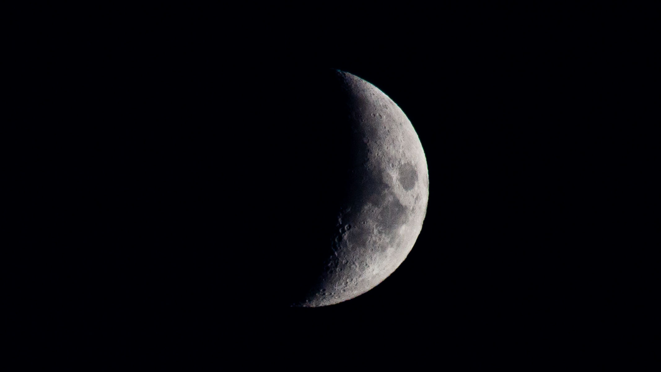 A large crescent moon in the night sky with some lunar seas and craters visible.