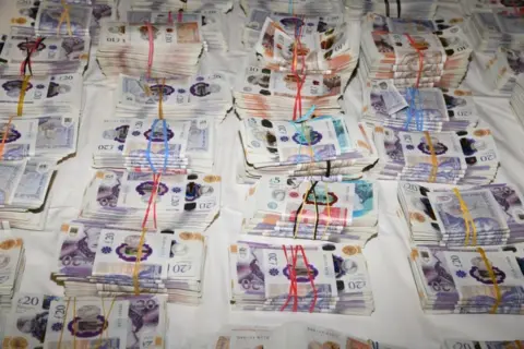 National Crime Agency Bundles of bank notes laid out over a white surface.