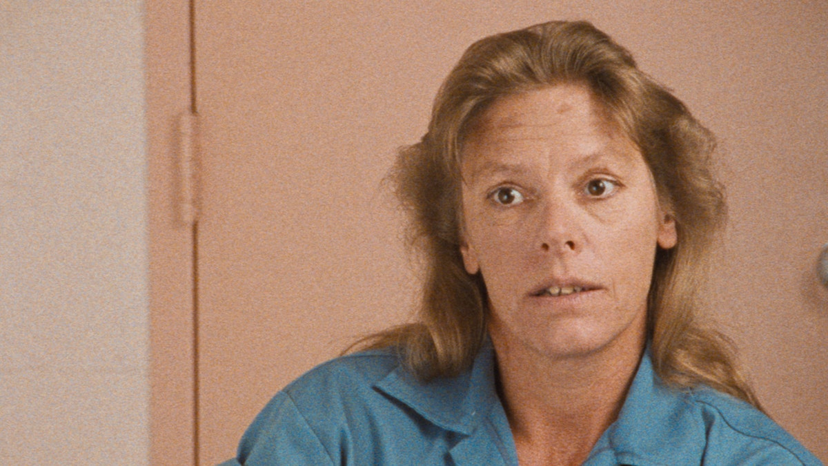 A close-up of Aileen Wuornos in conversation wearing a blue jumpsuit.