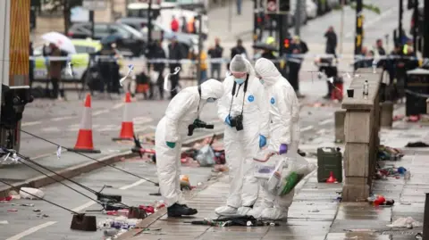 EPA Three forensics officers, wearing white overalls and blue masks, are at the scene where a car collided with fans during the Liverpool FC trophy parade in Liverpool city centre.